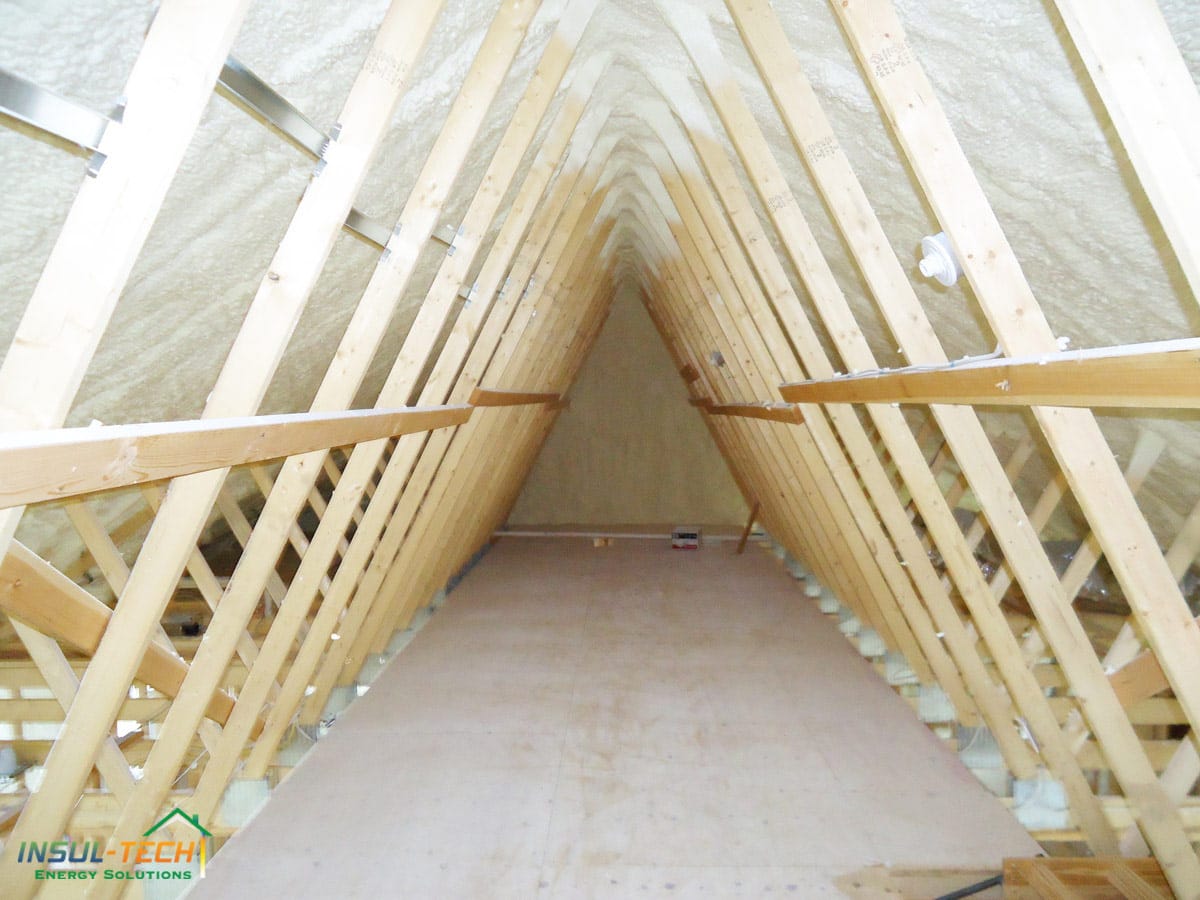 A close up of the inside of a roof with wooden beams and spray foam installed around the beams