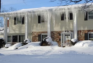 The side of a white house with icicles along the edge of the roof with a blue sky background